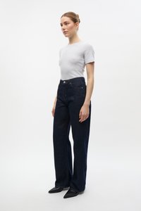 Hochtaillierte dunkle Jeans aus Denim mit geradem Bein, versehen mit sichtbaren Nähten, einem Knopfverschluss und einem Fünf-Taschen-Design. Kombiniert mit einem enganliegenden grauen T-Shirt.