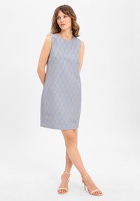 Robe sans manches bleu clair avec un motif géométrique doré. La coupe droite présente un col rond et arrive au-dessus du genou.