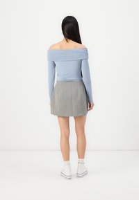 Svetlomodrý top s odhalenými ramenami a dlhými rukávmi, v kombinácii s šedou a bielou pruhovanou mini sukňou. Biely tenisky dotvárajú outfit.
