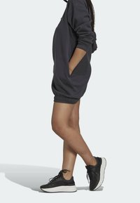 Mörkgrå överdimensionerad tröjdress med långa ärmar, sidofickor och elastisk fåll; kombinerad med svarta löparskor med vita sulor.