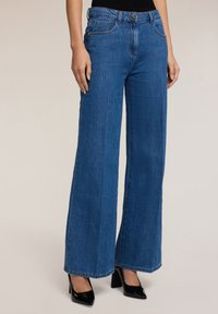 Pitkät siniset farkut leveillä lahkeilla ja korkealla vyötäröllä, joissa on etupainike, vyölenkit ja perinteiset takataskut. Tuntuva kankaantyöstö.