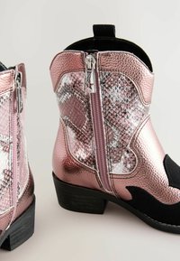 Roze metalik kauboj čizme s teksturiranim dizajnom zmijske kože. Crni antilop detalji i srebrni patentni zatvarač. Stepenasti potplat.