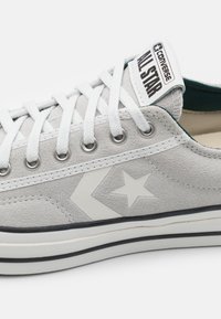 Grå mockaskor med vita detaljer, med en stjärnlogotyp, metallöglor och vita snören. Gummisula med svart och vit rand.