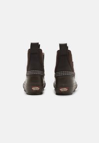 Tamsiai rudos Vans bateliai su elastingomis šoninėmis detalėmis, guminiais padais, baltais siuvinėjimo akcentais ir logotipo detalėmis kulne. Pateiktas galinis vaizdas.