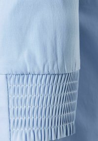Un tissu bleu clair présente une surface lisse avec une texture plissée le long de l'ourlet, mettant en avant un design extensible pour le confort.