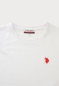 Tricou alb din bumbac, cu guler rotund și un mic logo brodat al U.S. Polo Assn. în culori roșii pe pieptul stâng. Textură netedă.