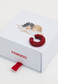 Rød ring besatt med rhinestone på en hvit boks med engelillustrasjoner og en rød trekkflik; "Fiorucci" logo i rødt på forsiden.