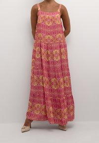 Maxi dress in pink with intricate gold patterns. Features wide straps and a tiered flowy design, made of lightweight fabric. Flat footwear visible.