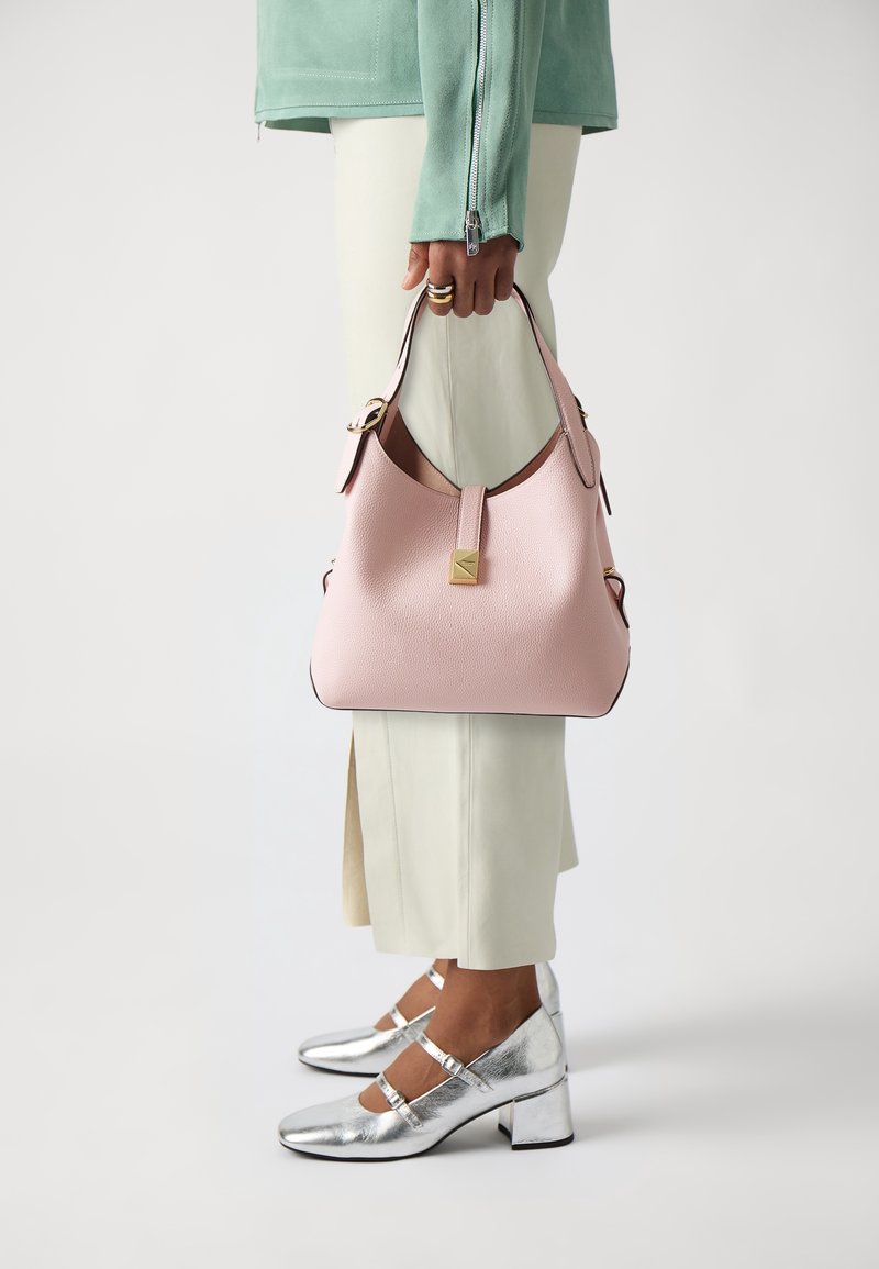 Roze lederen handtas met een afgeronde vorm, gouden accenten en een contrasterende donkere rand, gecombineerd met zilverkleurige metallic blokhak schoenen.