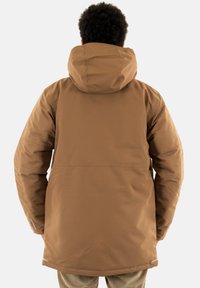 Chaqueta acolchada marrón con capucha. Presenta un diseño sencillo y una tela texturizada. Incluye puños elásticos y un acento reflectante en el dobladillo.