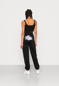 Černý zkrácený top bez rukávů s žebrovanou texturou v kombinaci s černými tepláky, které na zadní straně mají květinovou grafiku. Doplňují to bílé tenisky.