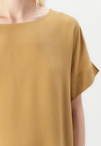 Sennepsgul kortermet topp laget av glatt stoff med rund hals og oppbrettede ermer, som har et enkelt og rent design.
