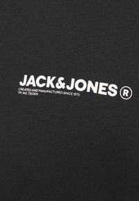 Zwarte katoenen t-shirt met witte tekst waarin "JACK & JONES" en "GECREëERD EN GEFABRICEERD SINCE 1975" staat in een vet, duidelijk lettertype.