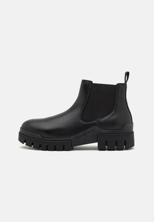 Bottes noires en cuir avec semelle épaisse, panneaux latéraux élastiques, languette de traction et marquage "Calvin Klein Jeans" sur la semelle.