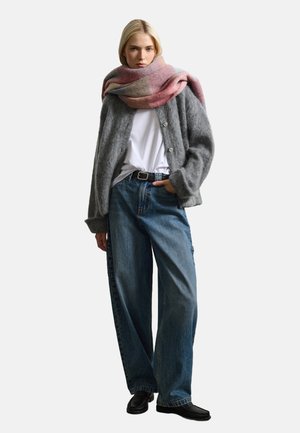 Cardigan en laine gris avec de grands boutons, t-shirt blanc, jeans en denim bleu ample et écharpe aux accents roses drapée autour du cou. Chaussures noires.