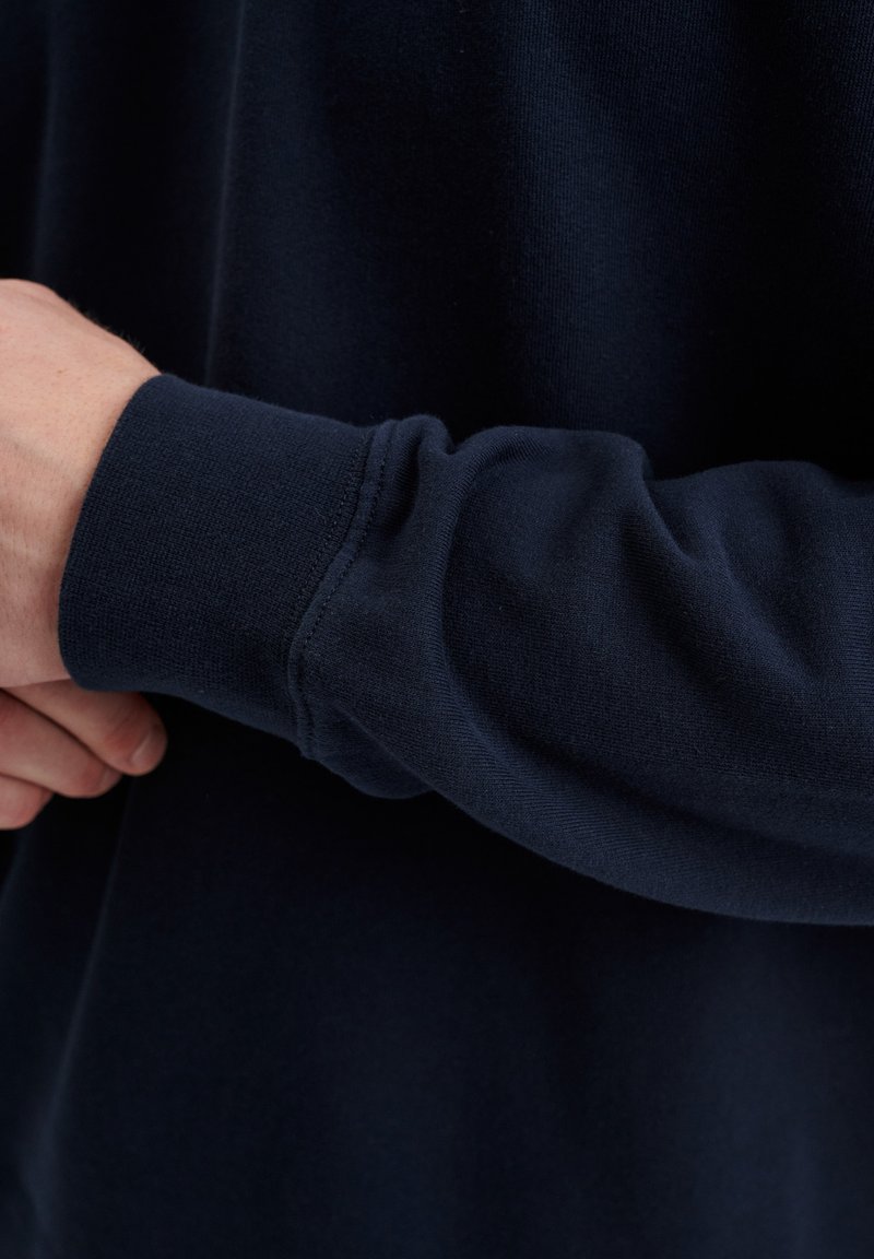 Navyblauwe sweatshirt met een zachte textuur en aansluitende manchetten, die een gladde, naadloze uitstraling toont met een subtiele stretch.