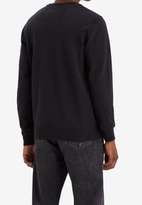 Sweatshirt noir avec un col rond classique, manches longues et poignets côtelés. Le tissu semble doux avec une texture lisse. Design minimaliste.