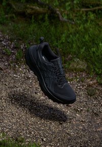 Black athletic shoe with a textured upper, reinforced toe, and cushioned sole. Features laces, logo detail, and a pull tab on the heel.