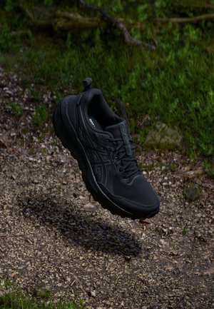 Schwarzer Sportschuh mit strukturiertem Obermaterial, verstärkter Zehenkappe und gepolsteter Sohle. Verfügt über Schnürsenkel, Logodetails und eine Zuglasche an der Ferse.