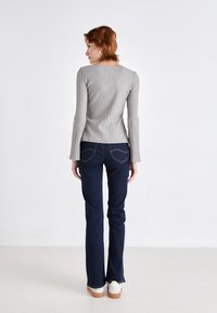 Top lungo grigio a coste con scollatura quadrata, abbinato a jeans svasati blu scuro. L'outfit presenta cuciture in vista e scarpe casual.