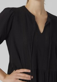 Vestido negro con escote en V, rayas verticales texturizadas, mangas abullonadas y cintura ceñida. Presenta costuras decorativas y lazos en el escote.