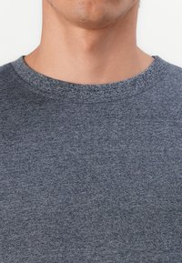 Maglione grigio con tessuto a trama, caratterizzato da un colletto rotondo e rifiniture a costine. Il materiale sembra morbido e informale.