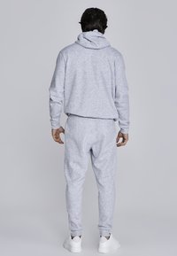 Gray cotton hoodie and joggers set, featuring a drawstring hood, ribbed cuffs, and matching elastic waistband, worn with white sneakers.