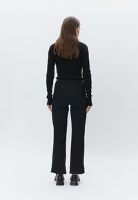 Black long-sleeve top and high-waisted black trousers, both fitted, with a slight flare at the hem and textural detailing on the fabric.