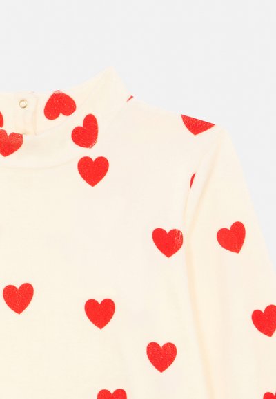 Bluză cu mâneci lungi, culoarea crem, cu modele de inimioare roșii și închidere cu capse la gâtul înalt.