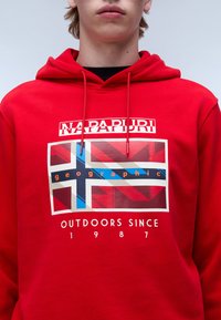 Sudadera de algodón roja con un diseño gráfico que incluye la bandera noruega, el texto "Napapuri" y la frase "geographic outdoors since 1987" en blanco.