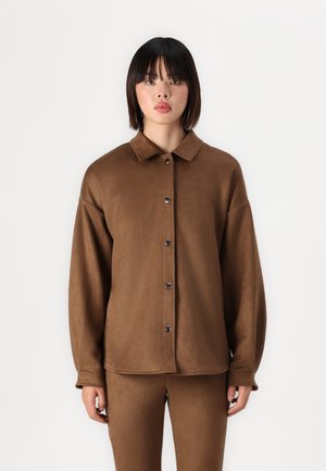 Brown, soft fabric shirt jacket with a collar, front buttons, and loose fit. Model shown wearing matching pants, with a smooth texture.
