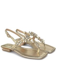 Gouden metallic sandalen met een platte hak. Voorzien van een T-band versierd met heldere edelstenen. Soepele textuur, vierkante neusontwerp.