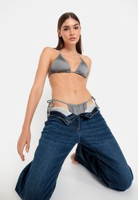 Un haut de bikini triangle en satin gris associé à un jean en denim bleu oversized, présentant une taille basse et des fermetures à liens sur les côtés.