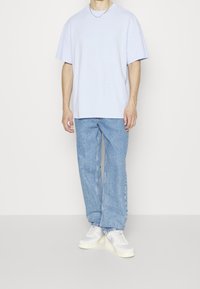 Světle fialové oversized bavlněné tričko kombinované se světle modrými rovnými džíny a bílými teniskami. Rukávy jsou krátké a volného střihu.
