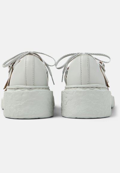 Białe platformowe trampki z teksturowaną, grubą podeszwą, widok od tyłu, zawiązane sznurowadła w kokardki oraz widoczne pionowe przeszycia na tylnych panelach.