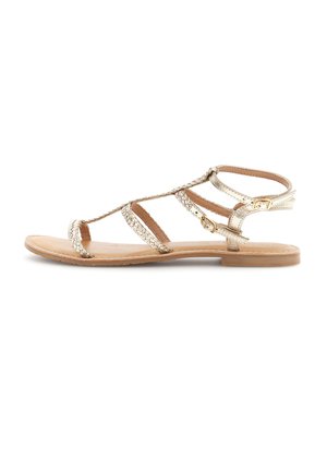 Sandalia plana con suela color marrón claro, tiras trenzadas metálicas doradas y dos pequeños cierres de hebilla dorada alrededor del tobillo.