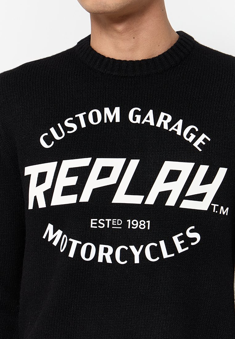 Schwarzer gestrickter Pullover mit kräftigem weißen Text: "CUSTOM GARAGE REPLAY ESTD 1981 MOTORCYCLES." Gerippter Ausschnitt, lässige Passform.