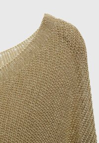 Gros plan sur un tissu en maille métallique dorée montrant un motif détaillé de boucles circulaires et un col côtelé sur un fond clair.