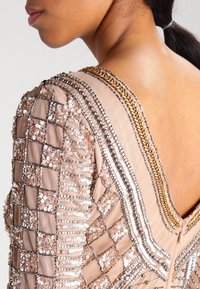 Pärlad klänning med rutmönster i ljusbeige, prydd med paljetter och silverdetaljer längs halsringningen och axlarna, med en jämn yta.