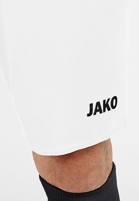 Weiße Sportshorts aus glattem Stoff mit einem schwarzen "JAKO"-Logo am linken Bein. Sie haben eine figurbetonte Passform und einen gesäumten Saum.