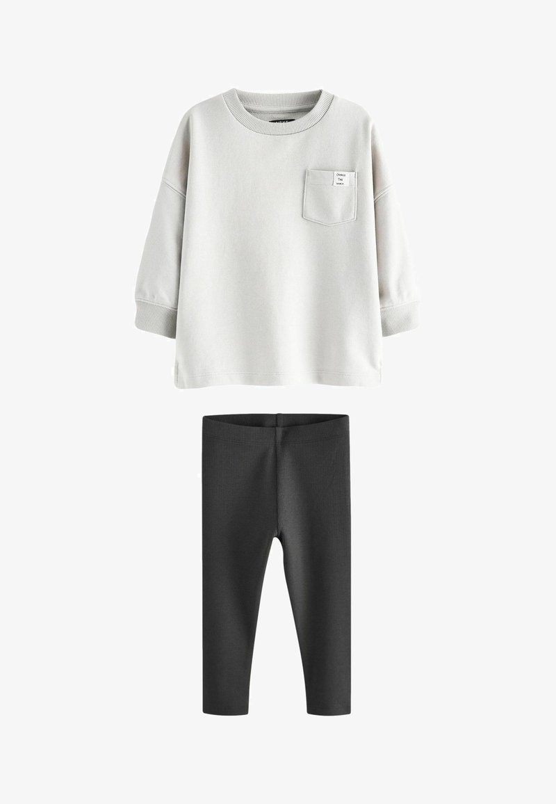 Gai pelēks krekls ar īsām piedurknēm un krūšu kabatu, apvienots ar melniem ribotiem legingiem, abi izgatavoti no mīkstas auduma.