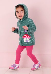 Zelená mikina na zips s bodkami, ozdobená červenými hubami a vílami, skombinovaná s ružovými legínami a multicolor teniskami.