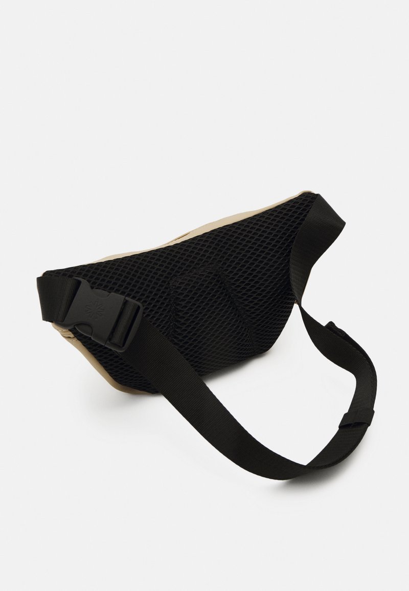 Sac de taille en maille noire avec une base beige, présentant un design texturé, une sangle ajustable et une boucle durable pour une fermeture sécurisée.