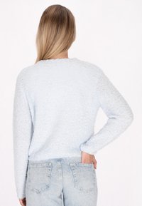Hellblauer Strickpullover mit texturiertem Finish, Rundhalsausschnitt und langen Ärmeln, kombiniert mit hellblauen Jeans.