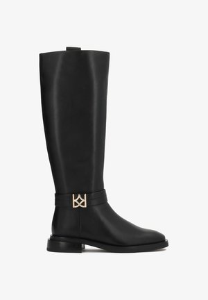 Bottes en cuir noires montantes avec un design épuré, semelle plate et un accent doré sur une sangle noire près de la cheville.