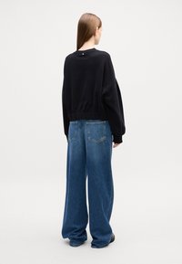 Felpa nera con vestibilità oversize e vita elastica, abbinata a jeans in denim azzurro a gamba larga con tasche posteriori. Elementi di design semplici.
