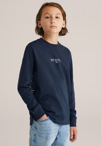 Námořnické triko s dlouhými rukávy vyrobené z jemné bavlny, s bílým grafickým motivem hor "Blue Ridge", uvolněný střih a žebrované manžety. Viditelné džíny.