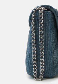 Denim axelväska med en strukturerad form, som har en silverfärgad kedjesnodd och textil med struktur. Den blå färgen är enhetlig med en subtil glans.