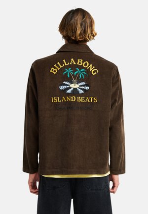 Osoba w brązowej kurtce sztruksowej z żółtym tekstem "Billabong Island Beats" oraz wzorem palm i winylowej płyty na plecach.