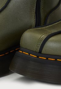 Bottine verte avec une finition texturée, dotée d'une fermeture éclair noire, de coutures d'accentuation noires et d'une semelle orange cousue avec une texture striée.